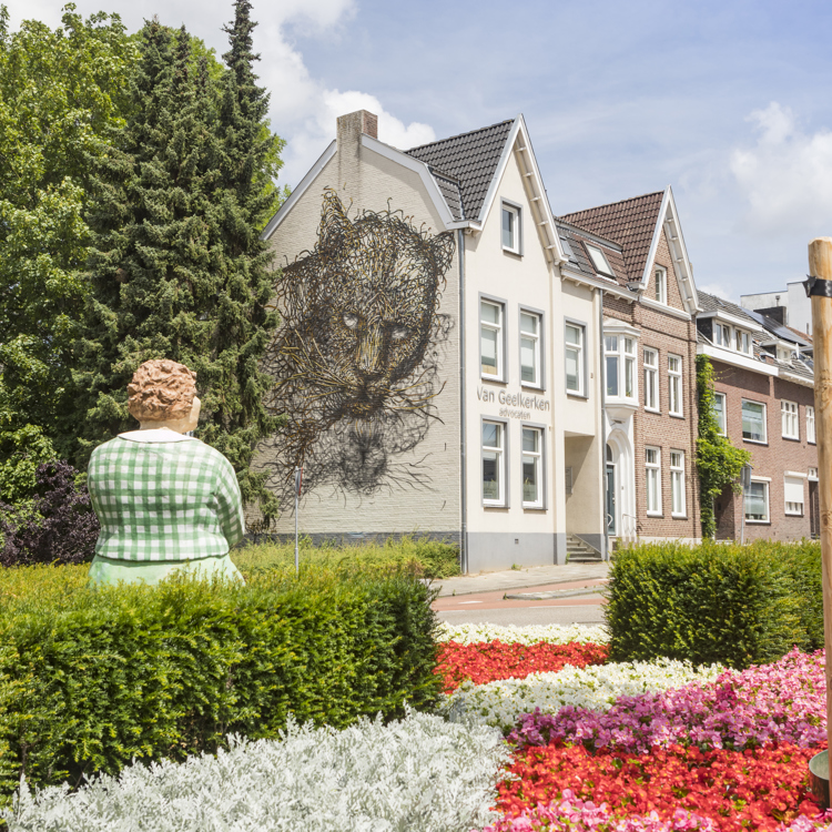 Een sculptuur van een alledaagse vrouw kijkt naar een grote mural van een zwarte katachtige op een gevel in Heerlen