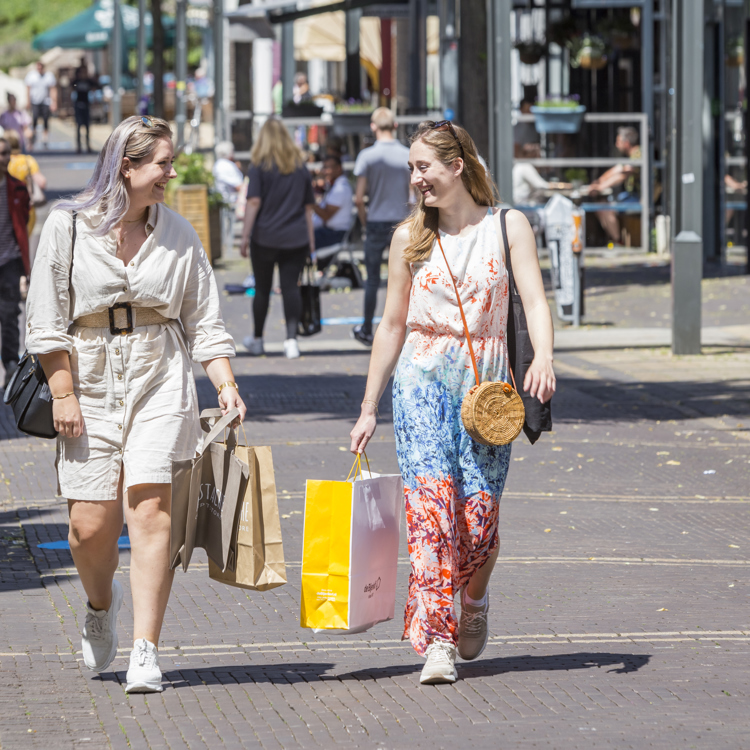 Twee meiden lopen al lachend met een winkeltasje door de winkelstraten van Heerlen