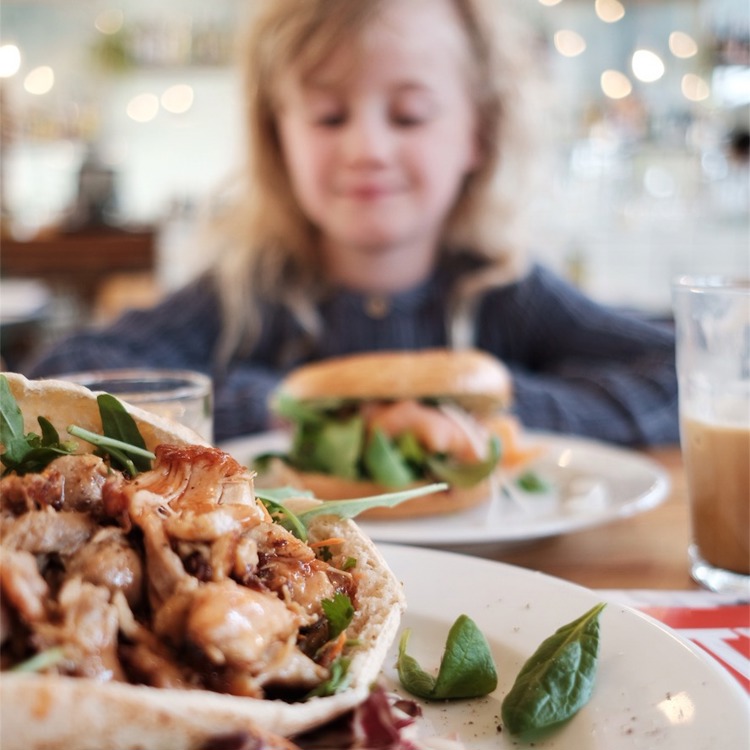 Detailopname van een kipgerecht, met op de achtergrond een kind die naar haar eten kijkt