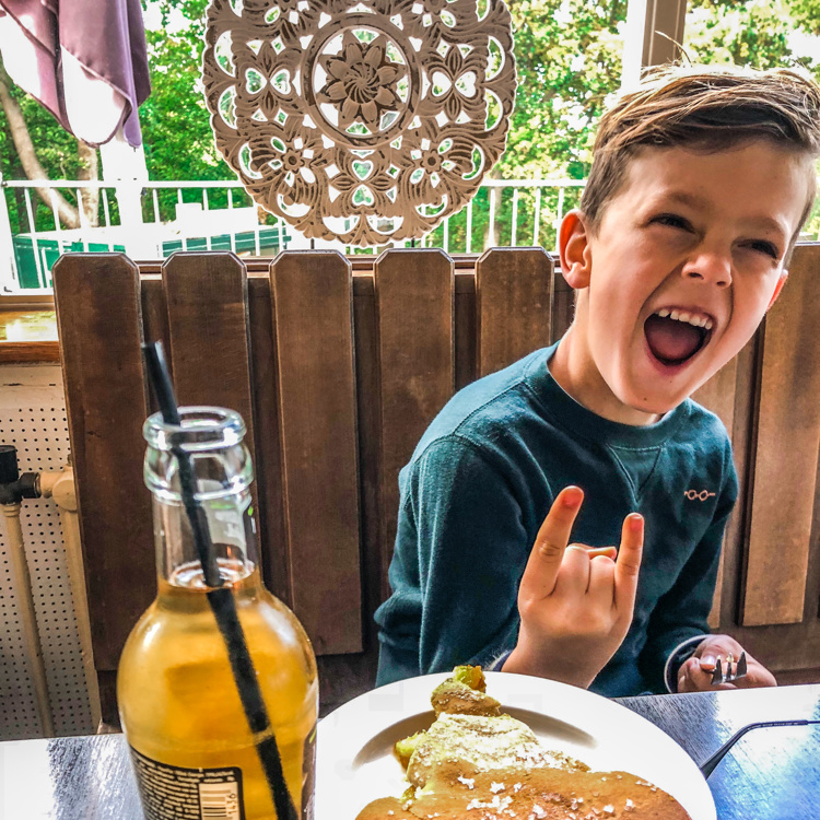 Een kleine jongen maakt een rockgebaar met zijn handen omdat hij geniet van zijn stuk vlaai en frisdrank