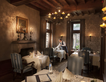 Een keurige serveerster dekt de klassieke tafels bij het restaurant van Kasteel Terworm