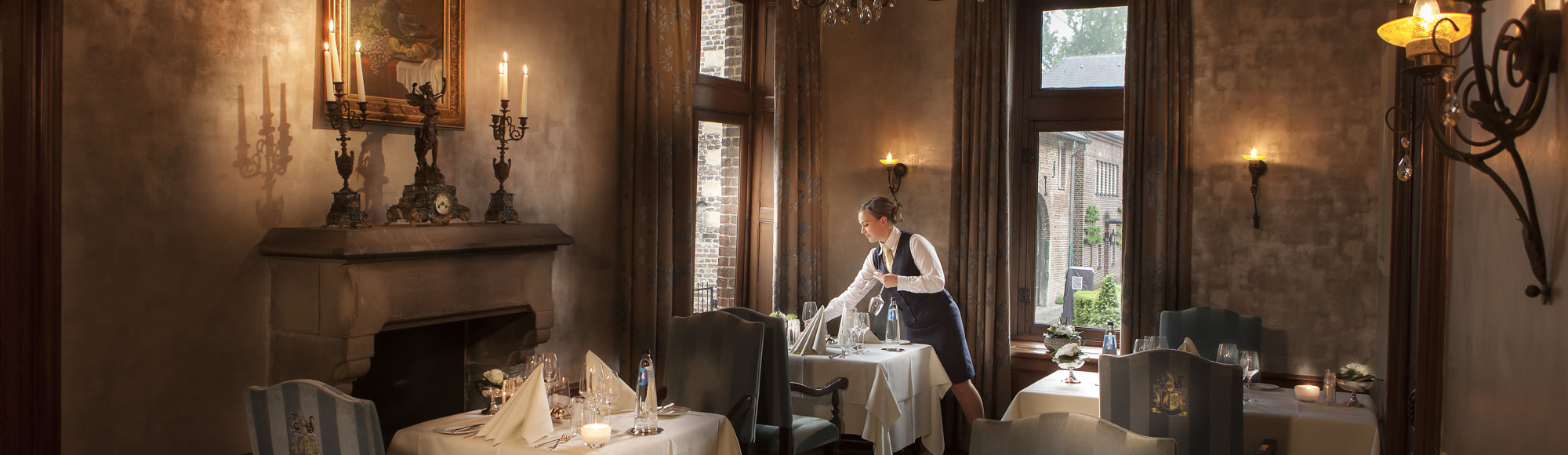 Een keurige serveerster dekt de klassieke tafels bij het restaurant van Kasteel Terworm