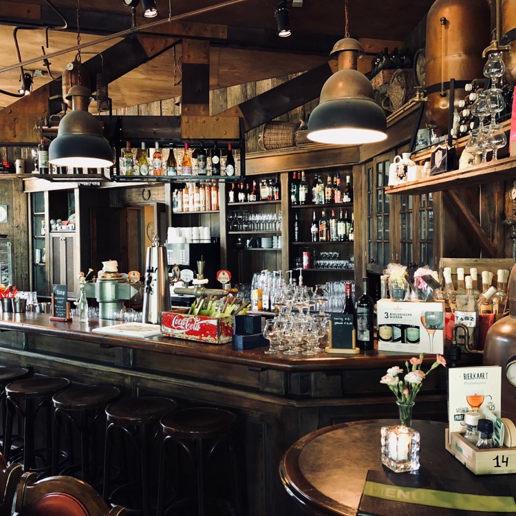 Een bruine bar met krukken en veel flessen drank op en rondom de bar