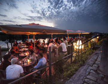 Groepen mensen zitten 's avonds op het terras aan de Maas met knusse verlichting en kaarsjes