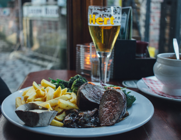 Een knus gedekt tafeltje met een bord vol friet, wild, en groenten, een uiensoep en een biertje