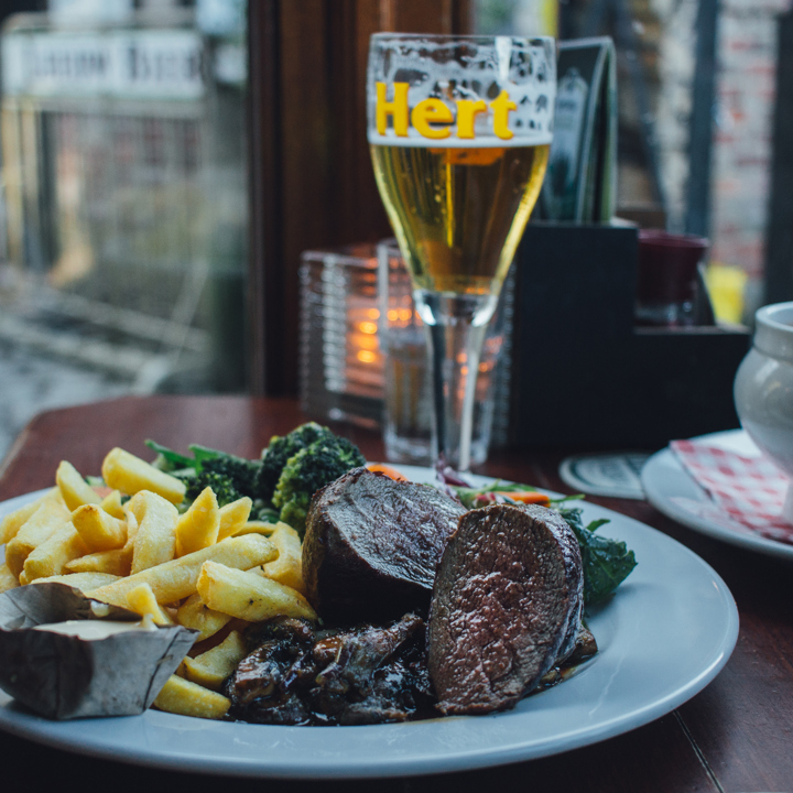 Een knus gedekt tafeltje met een bord vol friet, wild, en groenten, een uiensoep en een biertje