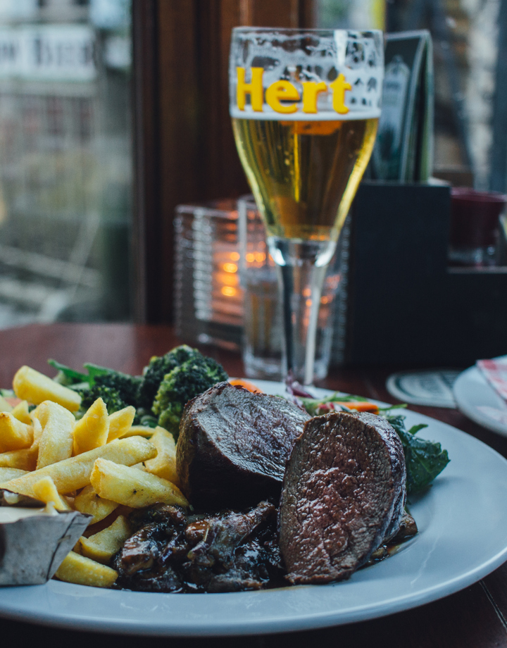 Een knus gedekt tafeltje met een bord vol friet, wild, en groenten, een uiensoep en een biertje