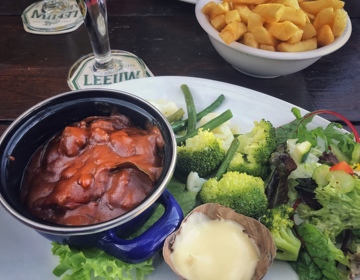 Een potje met zuurvlees, geserveerd met broccoli, boontjes en garnering