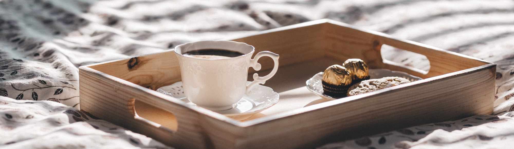 houten dienblad met koffie en bonbons op een hotelbed. 
