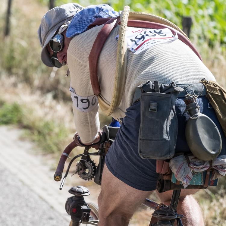 Man met ouderwetse wielerkleding en toebehoren kijkt achterom op oude wielrenfiets