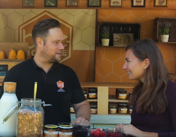 Een man en vrouw die staan te praten voor een kraam waar ze jam verkopen