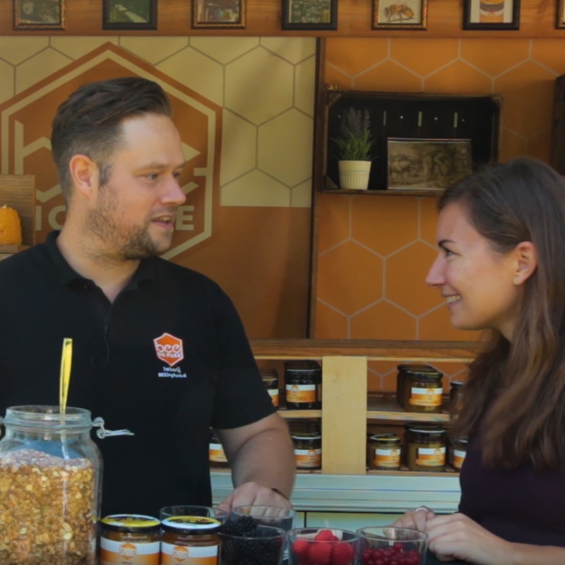 Een man en vrouw die staan te praten voor een kraam waar ze jam verkopen