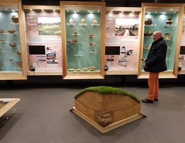 Meneer in tentoonstelling met urnen en informatiezuilen over grafstenen