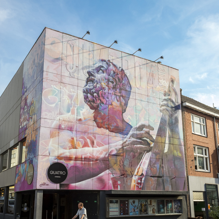 Zicht op Mural PichiAvo Orpheus Quatro Bioscoop Heerlen met fietsende persoon op de voorgrond