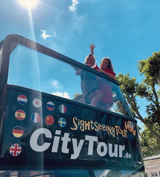 Vloggers Jenneke en Leonie zwaaiend vanaf het bovendek van de Hop on Hop off City tour bus