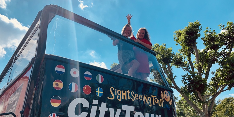 Vloggers Jenneke en Leonie zwaaiend vanaf het bovendek van de Hop on Hop off City tour bus