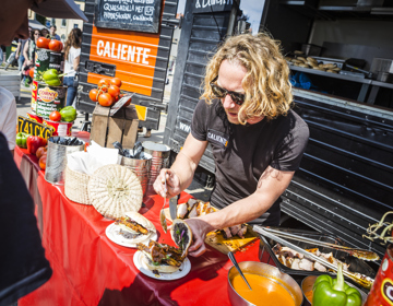 Een man met blond haar vult een culinair broodje met vlees