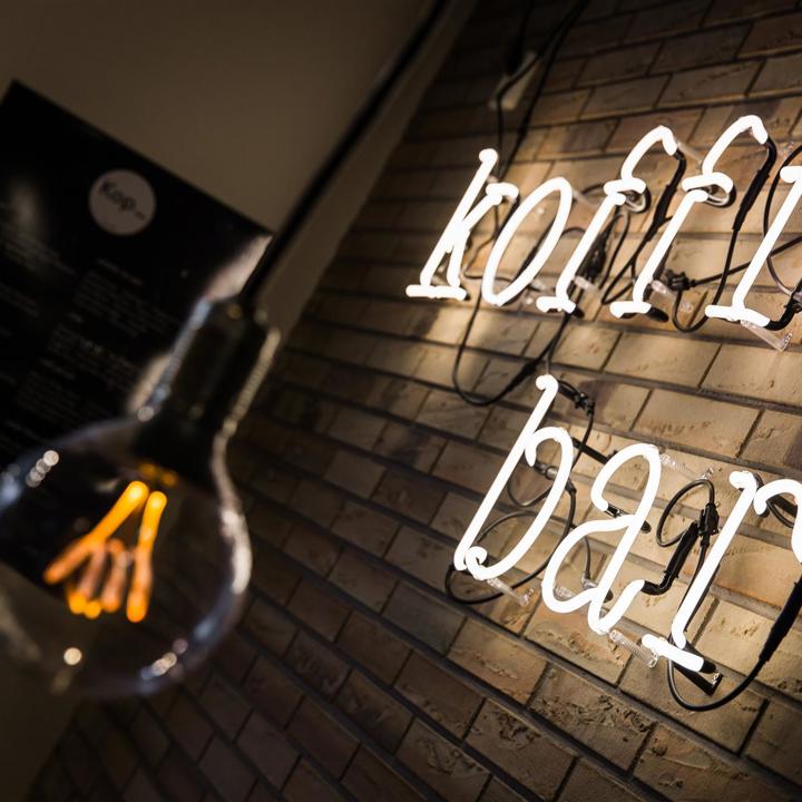 Verlichte gele neonletters die 'koffiebar' spellen en aan een muur hangen met op de voorgrond een gloeilampje