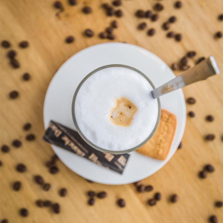 Een vers kopje koffie op een schoteltje met een koekje en suiker gezien van boven omringd met koffiebonen op een houten tafel
