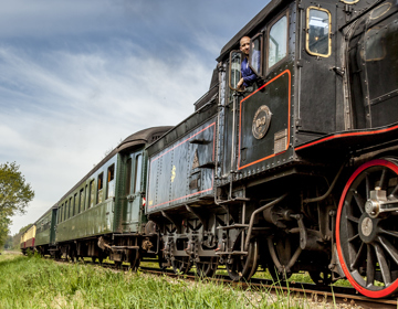 Zicht op de Miljoenenlijn Stoomtrein locomotief en treinstellen. Uit locomotief hangt de machinist. 