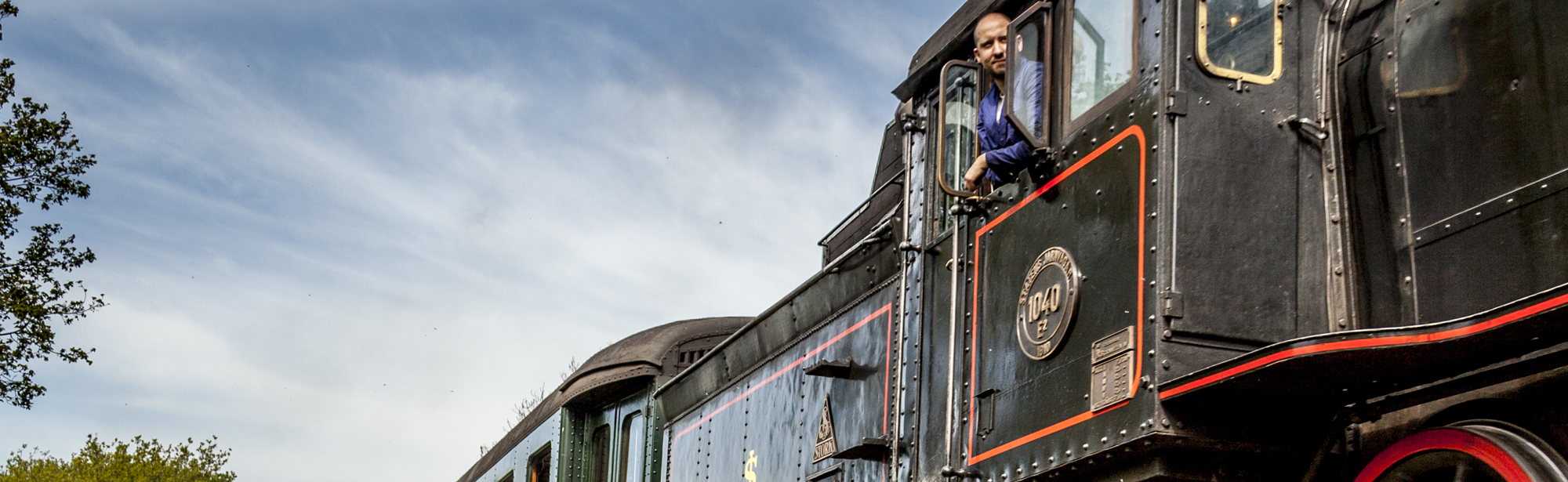 Zicht op de Miljoenenlijn Stoomtrein locomotief en treinstellen. Uit locomotief hangt de machinist. 