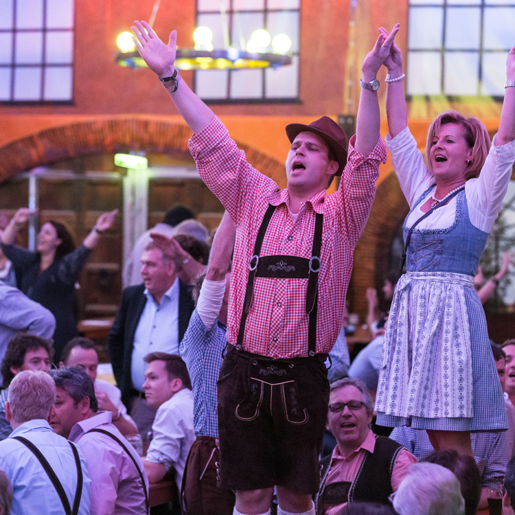 Man en vrouw in tiroolse outfit staan op bank met handen in de lucht tijdens Oktoberfest in Sittard