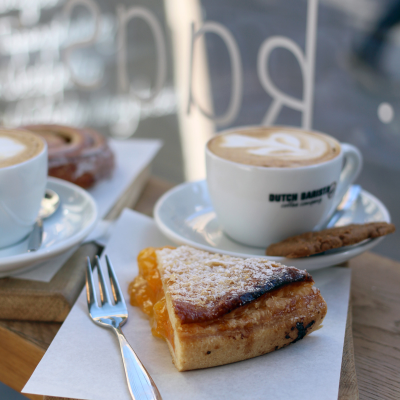 Een stukje abrikozenvlaai met een kopje koffie achter een raam van een lunchcafeetje