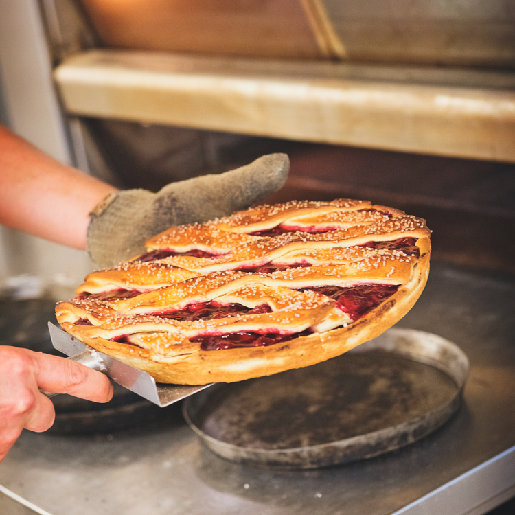 Een man met schep houdt een kersenvlaai vast voor een bakoven