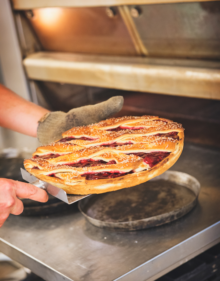 Een man met schep houdt een kersenvlaai vast voor een bakoven