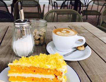 Een stuk carrot cake en kopje koffie geserveerd op het terras