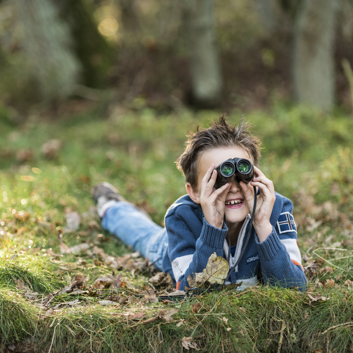 Jongetje ligt in het gras tussen de bladeren met een verrekijker