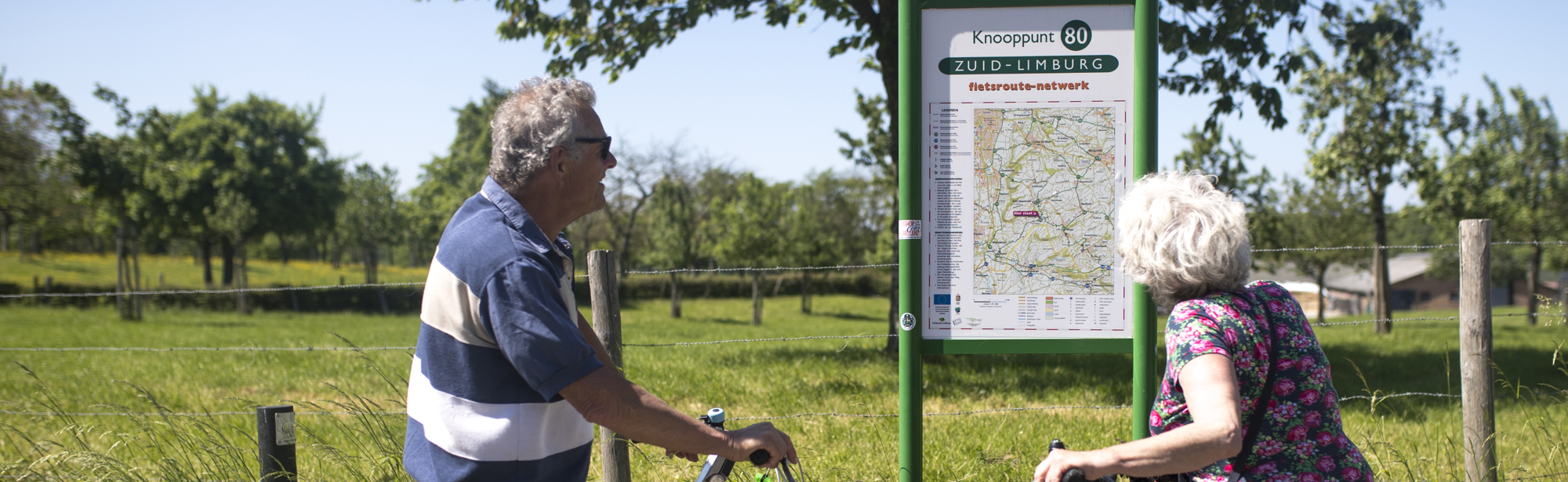 Twee ouderen mensen met fiets in hun hand kijken naar een infopaneel met fietsknooppunten