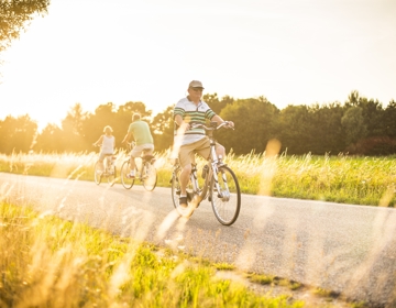 Een oude man fietst over een verharde weg op een zonnige avond