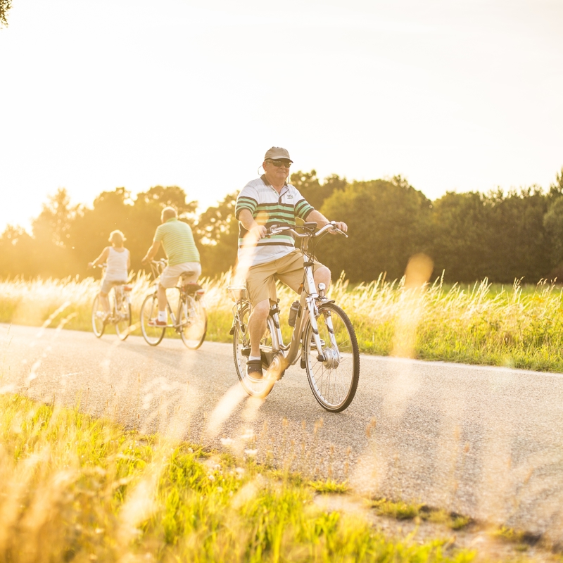 Een oude man fietst over een verharde weg op een zonnige avond