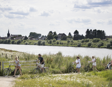 Een groep fietsers en een scooter zijn net de Maas overgestoken en lopen tot aan het pad