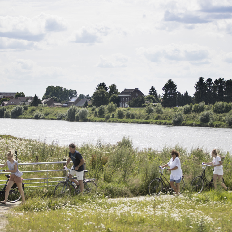 Een groep fietsers en een scooter zijn net de Maas overgestoken en lopen tot aan het pad