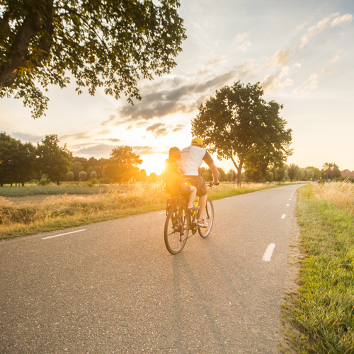Een man met een kindje fietst op een zonnige avond over de weg