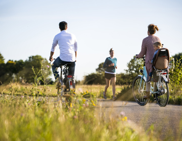 Een gezin fiets over een harde weg langs een hardlopende vrouw