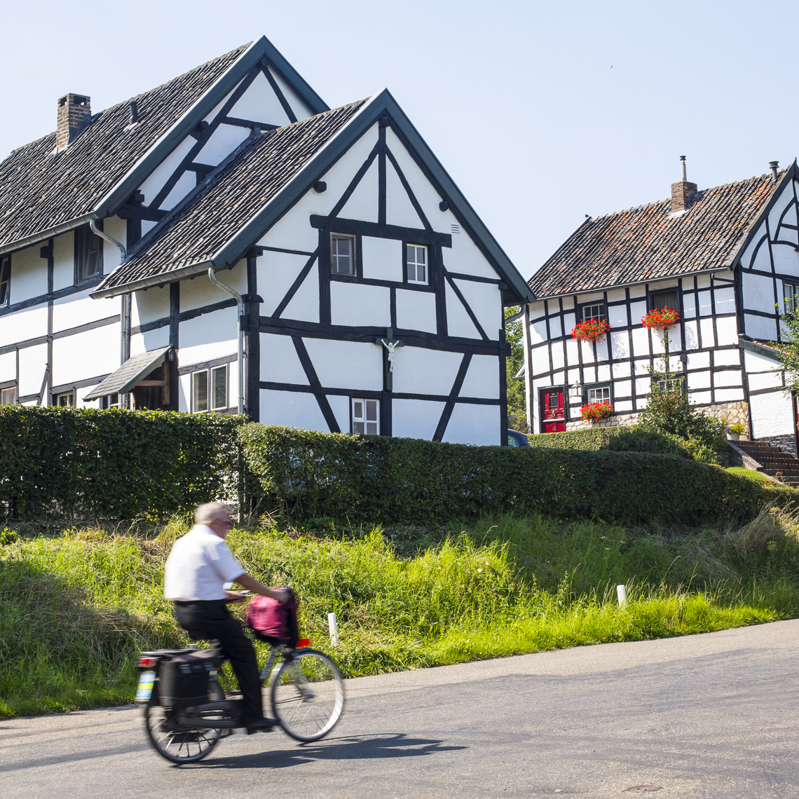 Een oude man fietst langs twee vakwerkhuizen