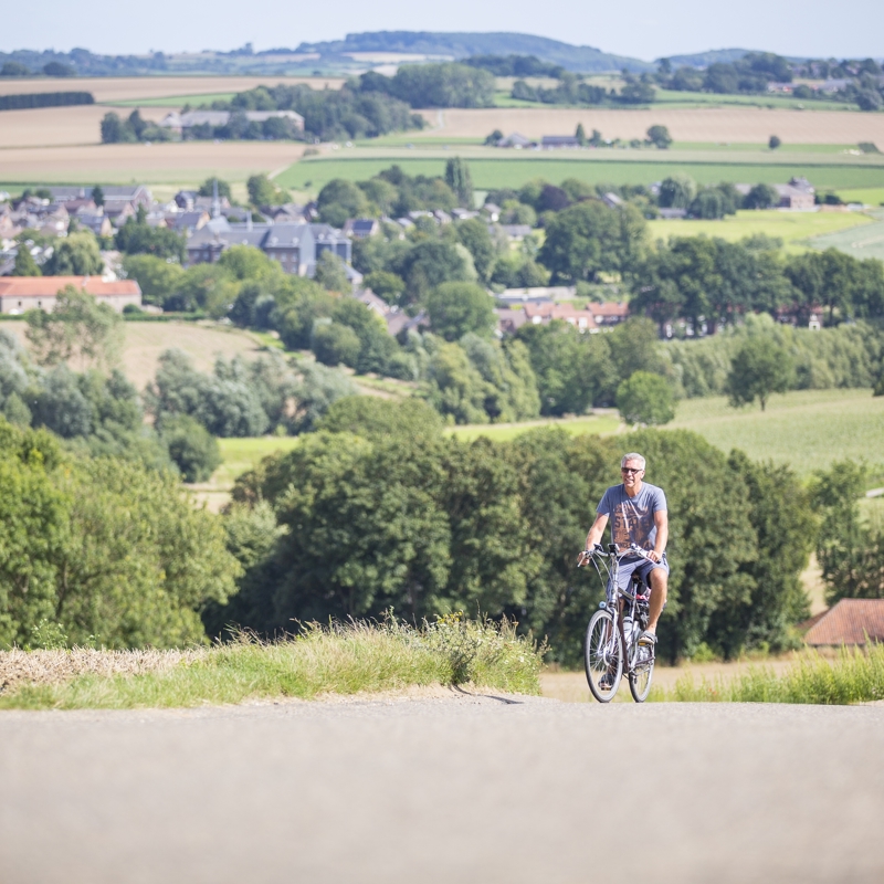 Een fietser beklimt een steile berg in het Heuvelland met prachtig panorama achter zich