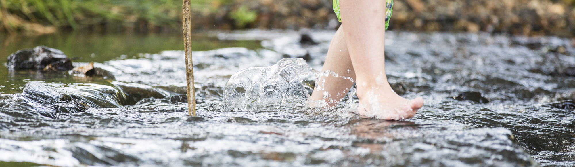 Kind loopt met blote voeten door het water met een stok