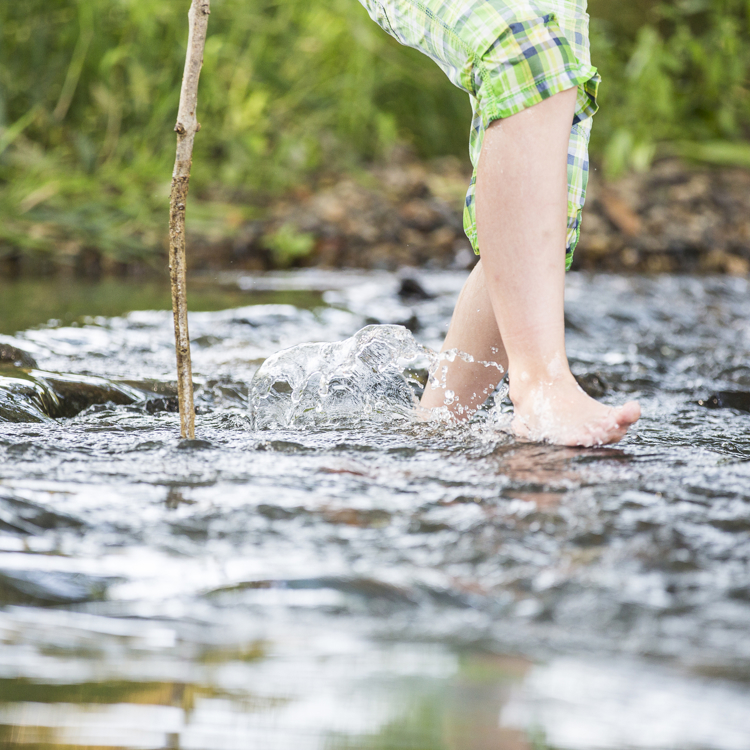 Kind loopt met blote voeten door het water met een stok