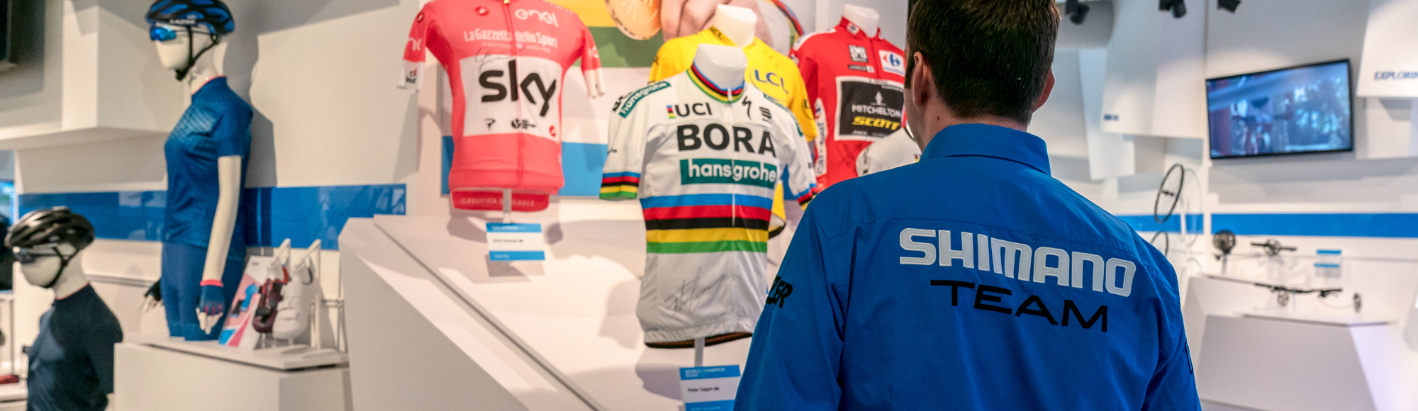 Man met Shimano vest kijkend naar borstbeelden met wielershirts van kampioenen in Shimano Experience Center