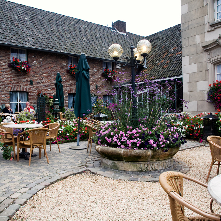 Een kleurrijke binnenhof vol bloemen en terrastafeltjes bij een oude boerderij