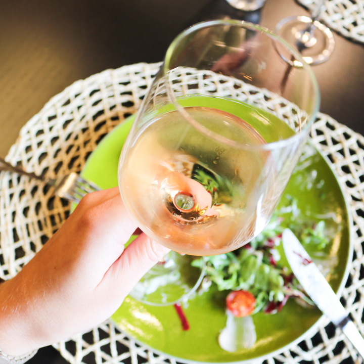 Een glas rosé wordt de lucht in gehouden boven een dinerbord met salade