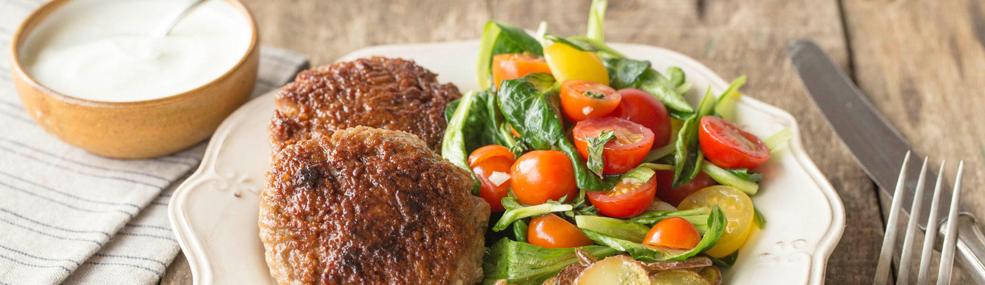 Livar lende gehaktballen geserveerd op een bord met aardappeltjes en salade met tomaten en een bakje saus