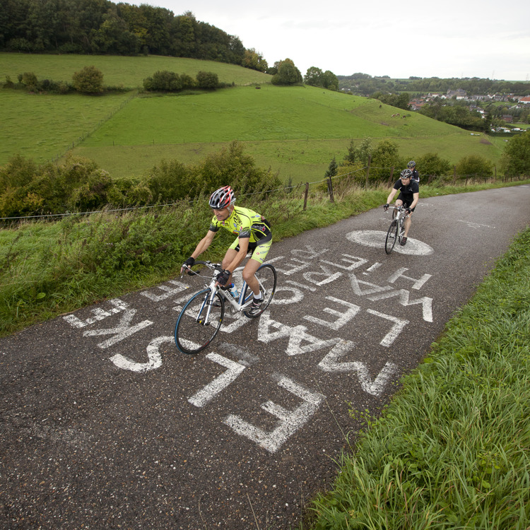 Verschillende wielrenners beklimmen de Keutenberg met tekst geschreven op de weg
