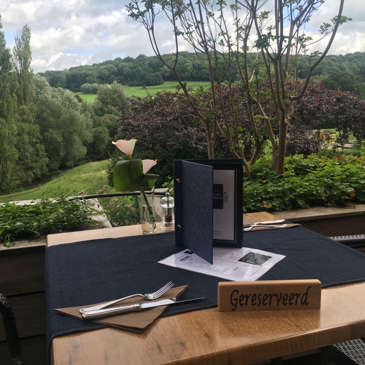 Gedekt tafeltje op een terras met gereserveerd bordje en uitzicht over de zuid-limburgse heuvels. 