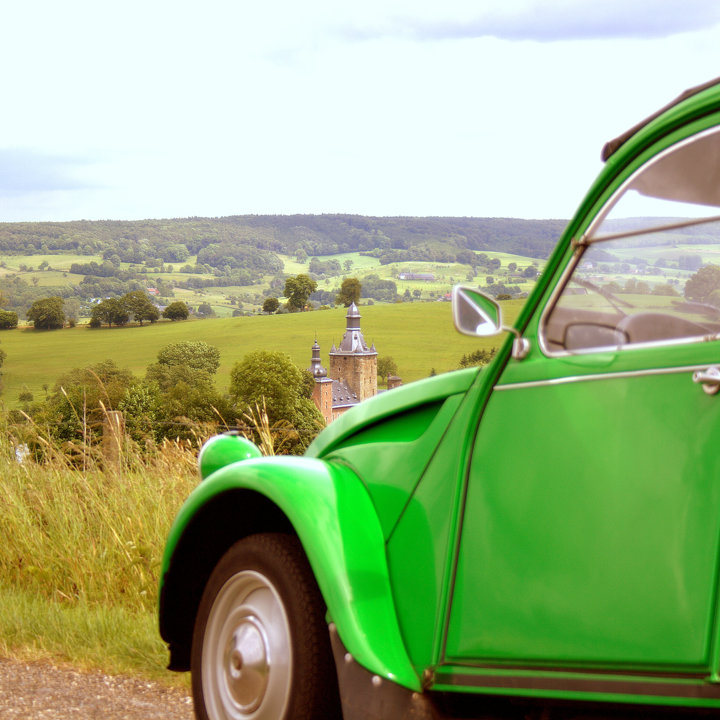 Een groene auto, ook wel een eend genoemd, staat geparkeerd langs de weg met uitzicht over het heuvelland