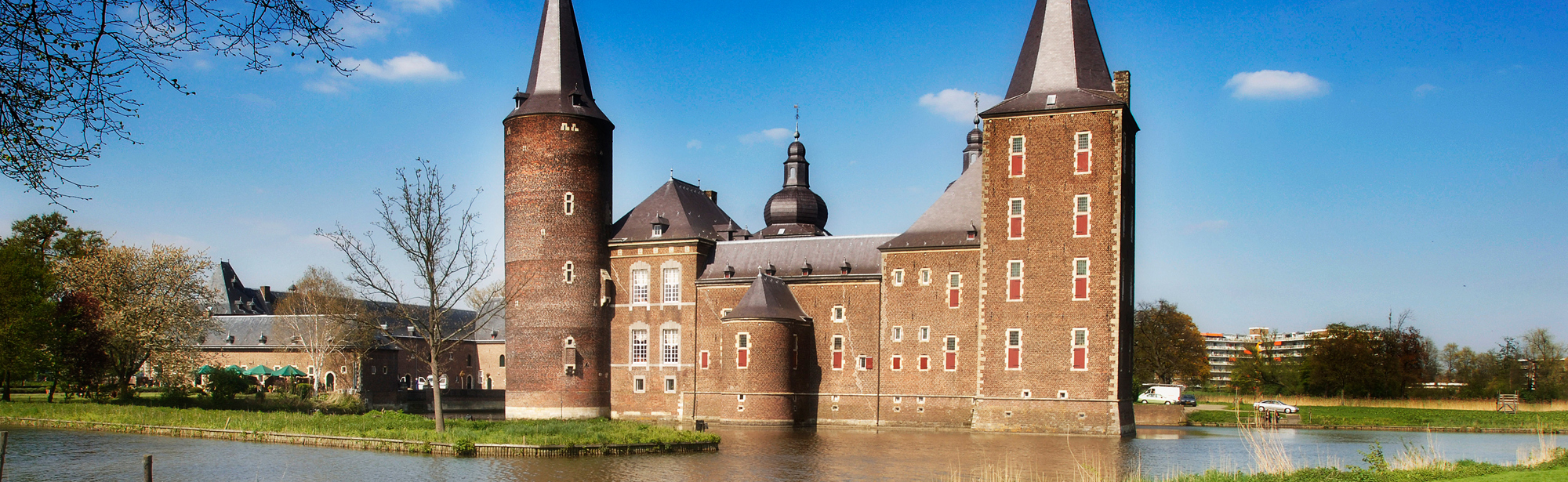 Eentjes lopen op het het gras met daarachter water en Kasteel Hoensbroek